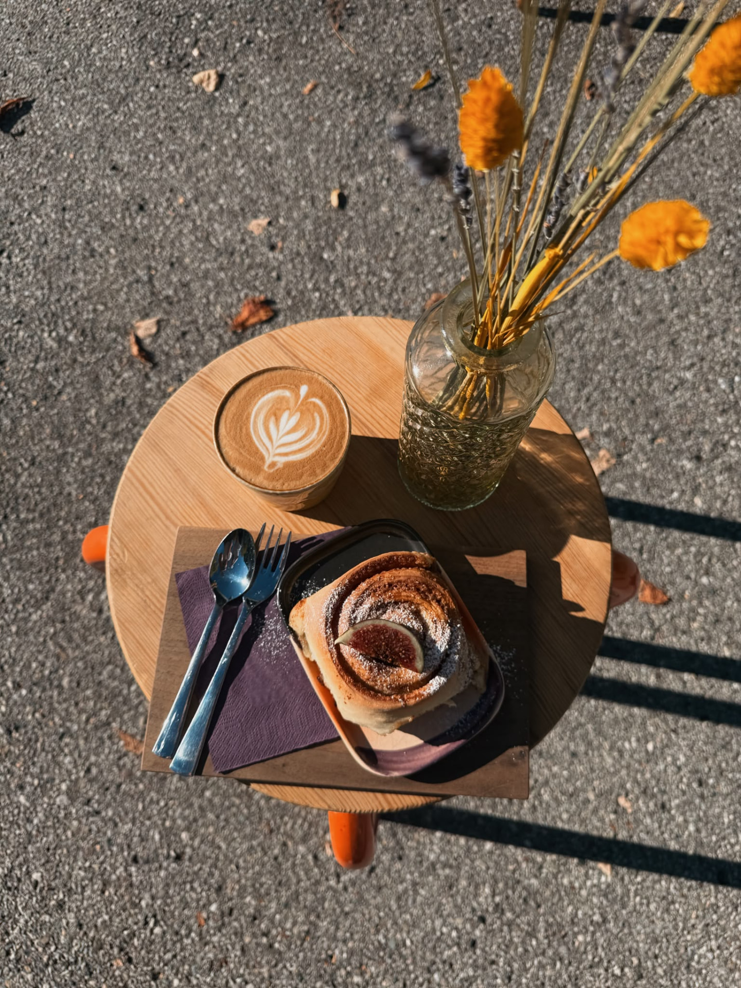 Kaffee mit Latte Art und eine Zimtschnecke auf einem kleinen Holztisch